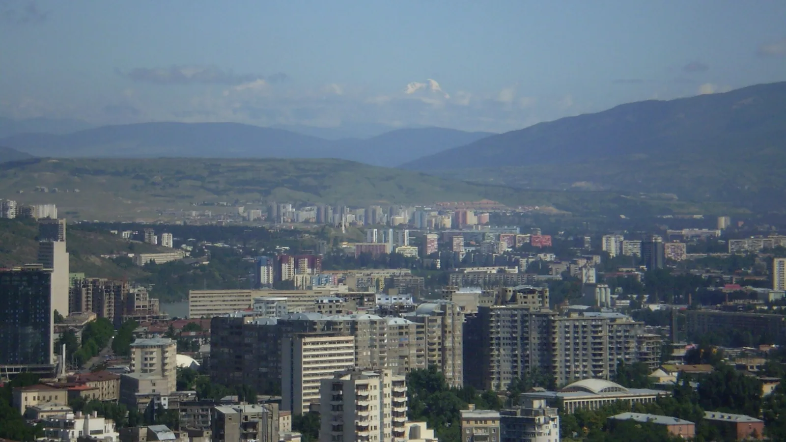 Tbilisi cityscape seen from above with mountains and clouds beyond the city