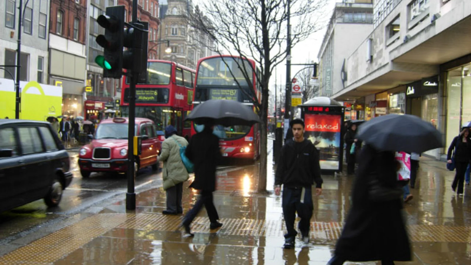 People carrying umbrellas beside buses and taxis on Oxford Street in London during rain